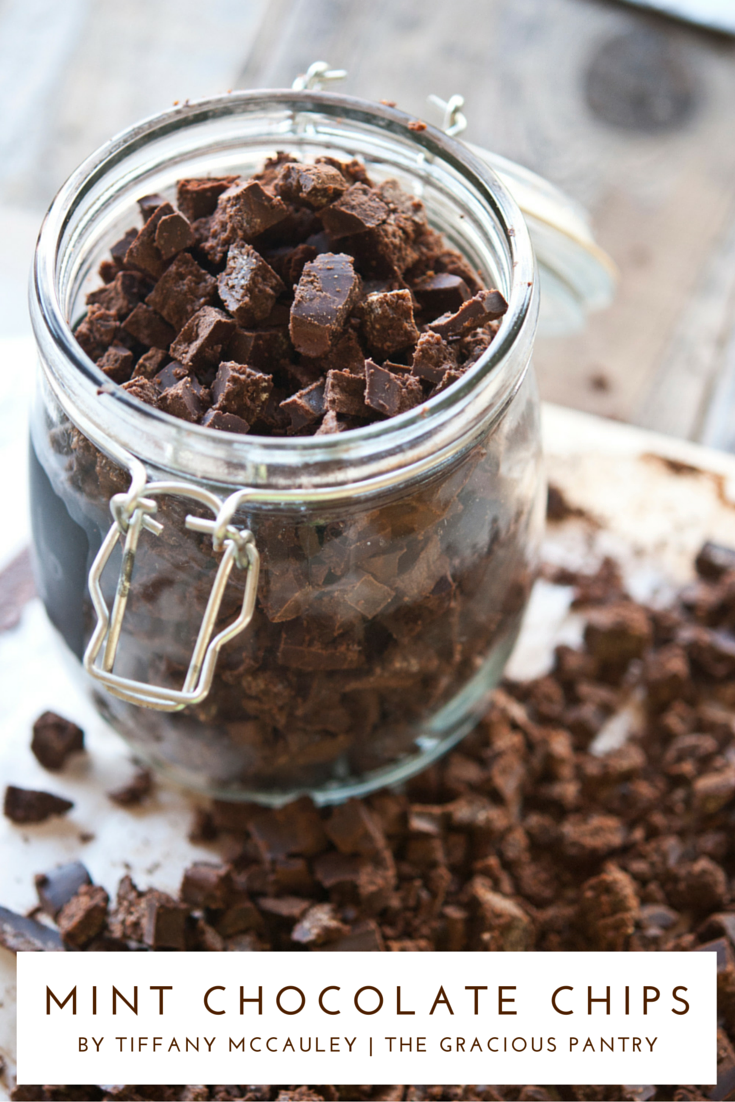 Clean Eating Homemade Mint Chocolate Chips in a glass storage jar. The lid is off so you can see the chocolate chips inside. There are also lots of chocolate chips outside the jar, surrounding the base.