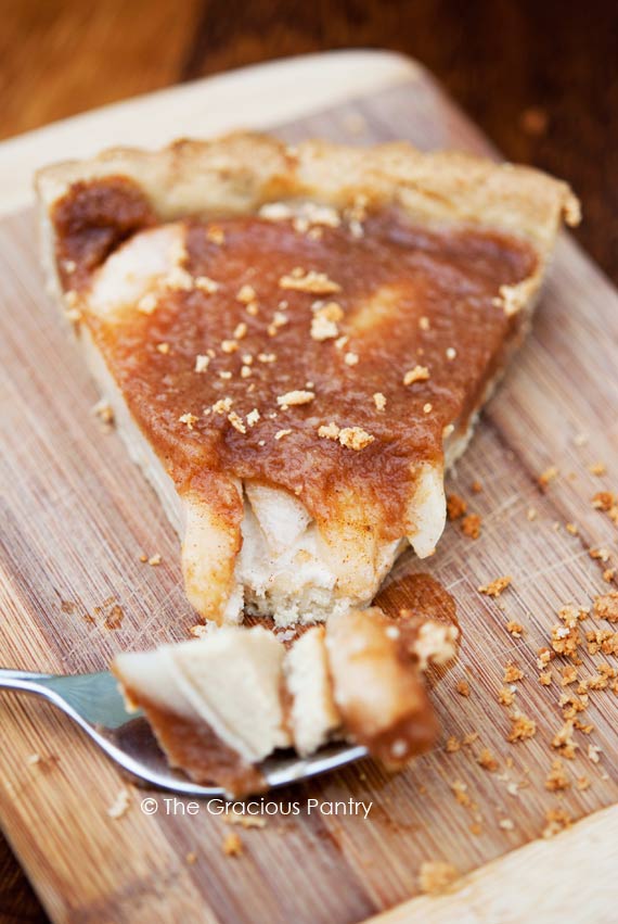 A slice of Pear & Apple Tart sits on a wooden surface with a fork-full sitting in front of it.