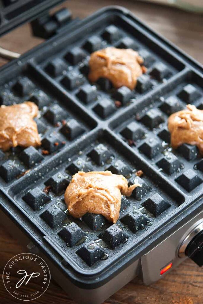 Dollops of dough in the center areas of waffle squares on a waffle iron.