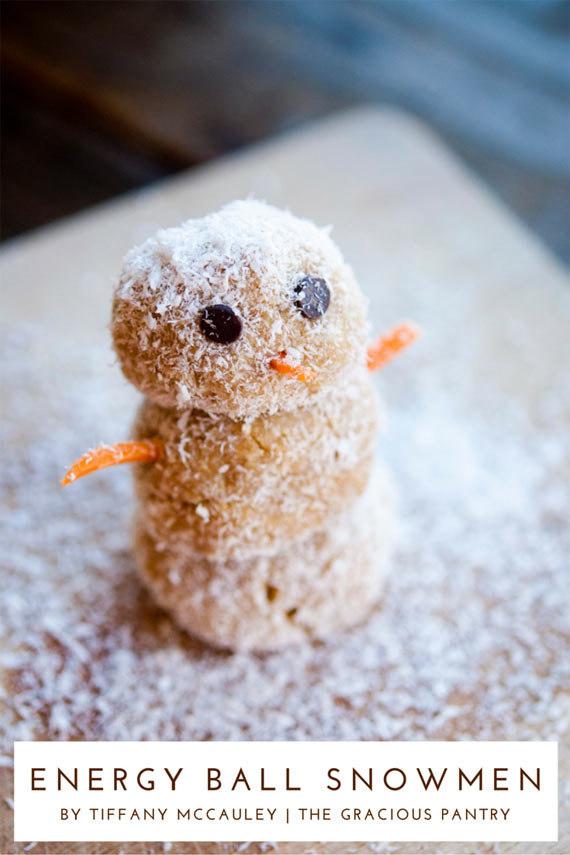 A single snowman sites on a cutting board with coconut flakes sprinkled all around him. It looks like he's sitting in snow. This is what this recipe for Clean Eating Energy Ball Snowmen will look like when it is done.