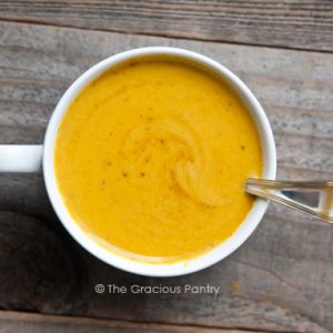 An overhead view of a white mug filled with easy Curried Pumpkin Soup, with a spoon resting in the soup on the side of the mug.