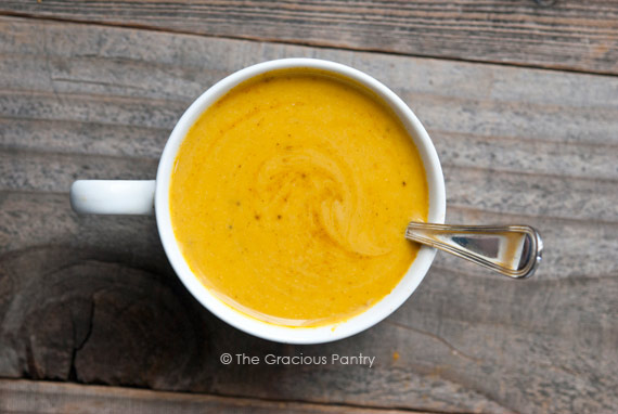 An overhead view of a white mug filled with easy Curried Pumpkin Soup, with a spoon resting in the soup on the side of the mug.