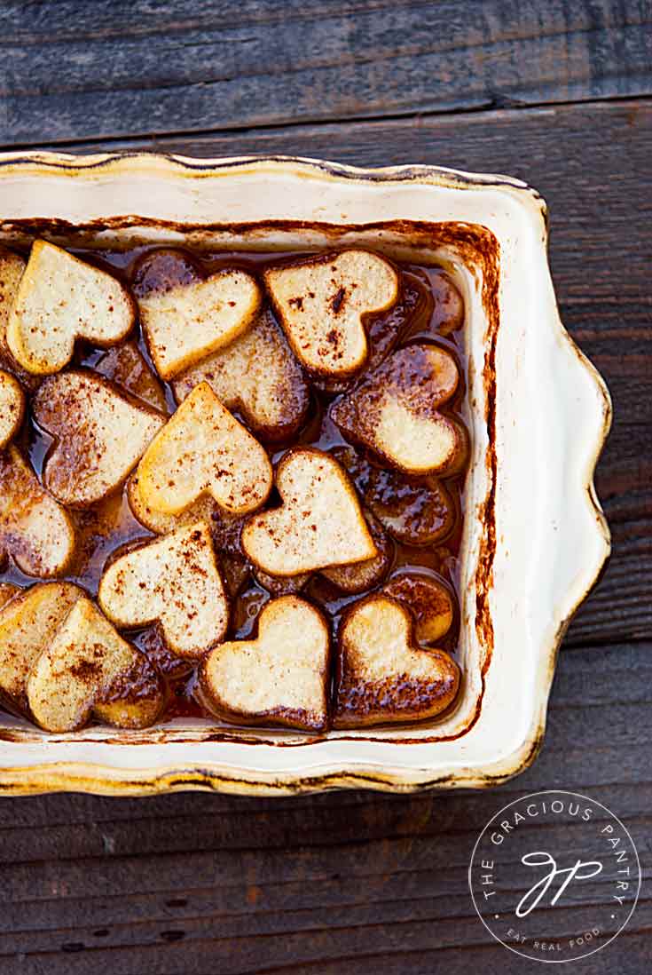 Maple Baked Sweet Potatoes cut into hearts and sitting in a casserole dish, covered in maple syrup.