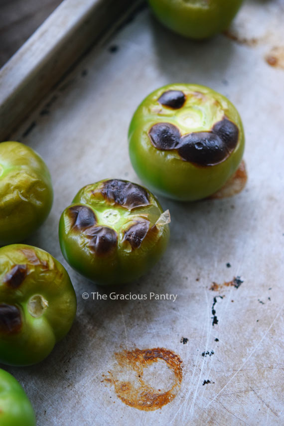 Several tomatillos on a baking sheet that have blistered tops from being roasted.