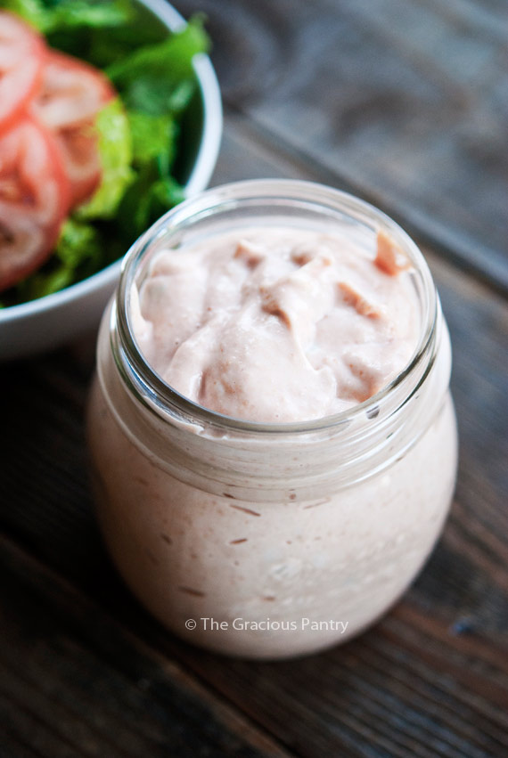 Clean Eating Thousand Island Dressing in an open jar, next to a bowl of lettuce and tomatoes.