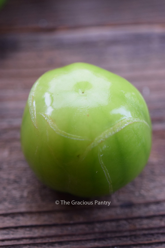 A tomatillo with the husk removed showing cracks in it's shiny green skin depicts a tomatillo which should not be purchased.