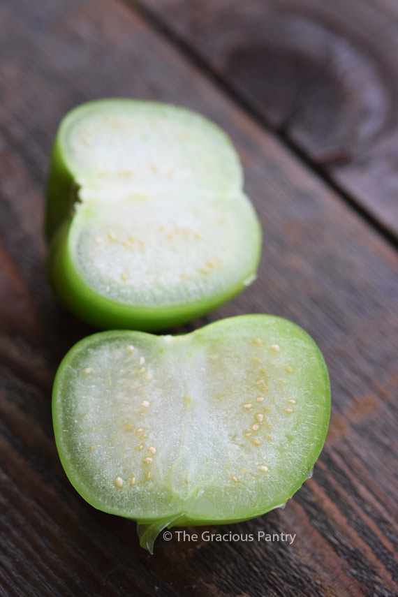 A tomatillo cut in half, showing it's white insides with small yellow seeds.