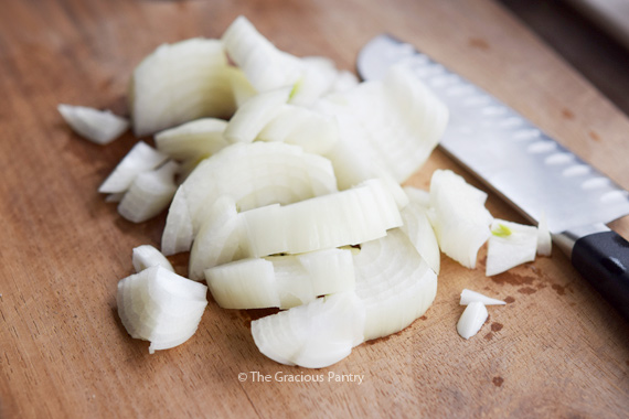 Chopped onions lay on a cutting board next to a knife.
