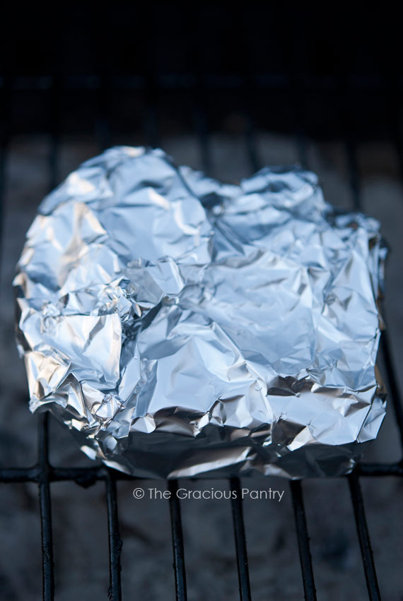 A Campfire Grilled Cheese Sandwich, wrapped in foil and laying on a black grill.