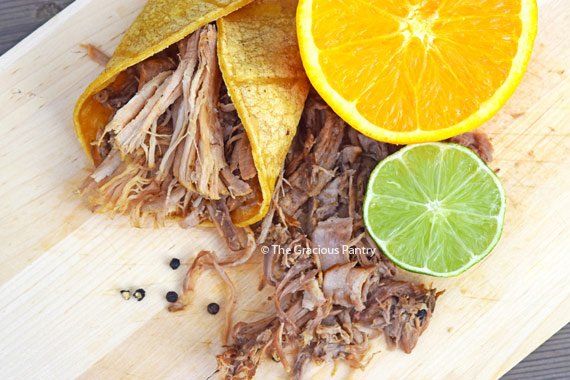 An overhead view looking down on a Slow Cooker Carnita laying on a cutting board with an orange and lime.