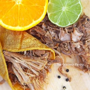 An overhead view looking down on Slow Cooker Carnitas laying on a cutting board with a cut orange and lime.