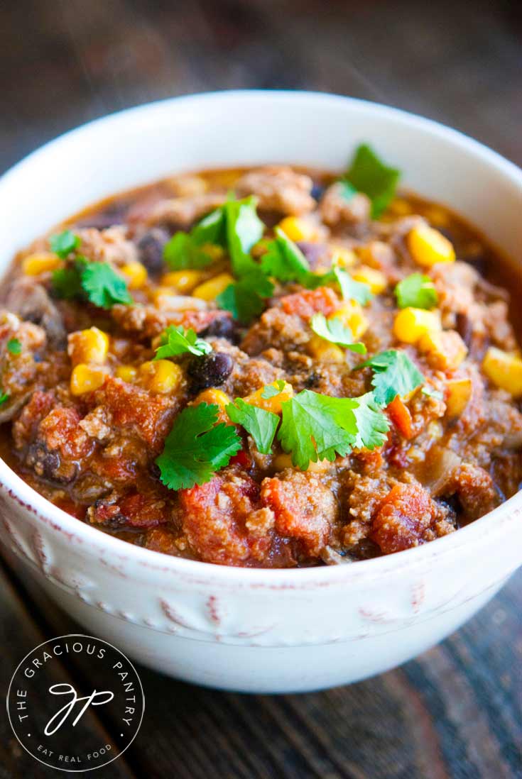 An off white bowl sits on a dark wood surface filled nearly to the top with Clean Eating Southwestern Turkey Chili.