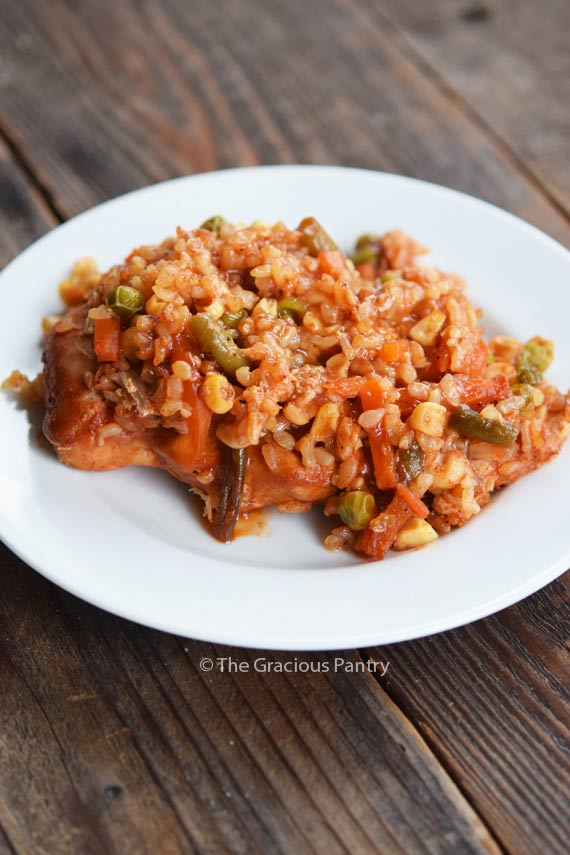 A single plate of this Clean Eating Barbecue Chicken Casserole shows a single chicken breast topped with barbecue sauce and mixed vegetables with brown rice, all layered onto of each other.