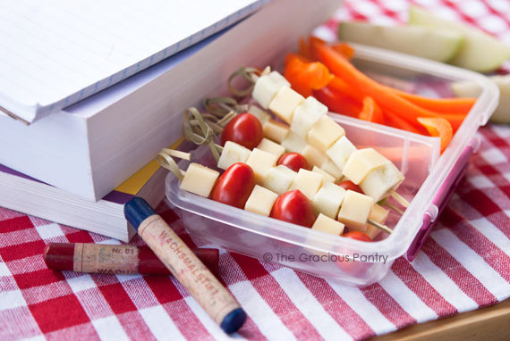A lunchbox container filled with lunchbox kebobs sits next to some books and crayons.