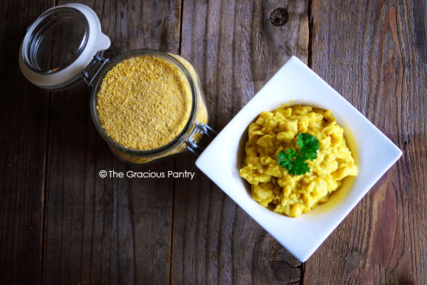 Clean Eating Macaroni & Cheese Dry Mix Recipe shown from overhead. The image includes the dry mix in a clear jar standing next to a white bowl of prepared macaroni and cheese.