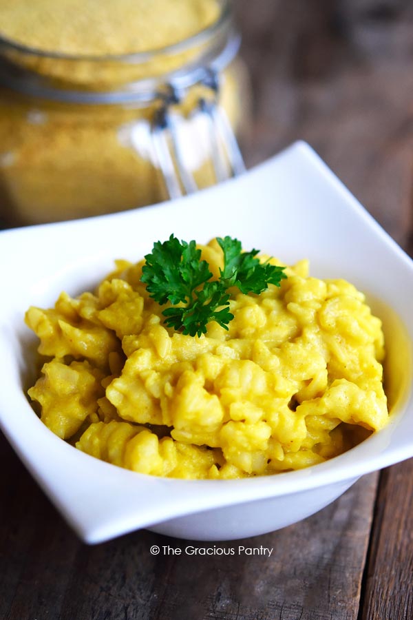 Clean Eating Macaroni And Cheese Dry Mix shown in a jar sitting just behind a white bowl of deliciously, golden macaroni and cheese.