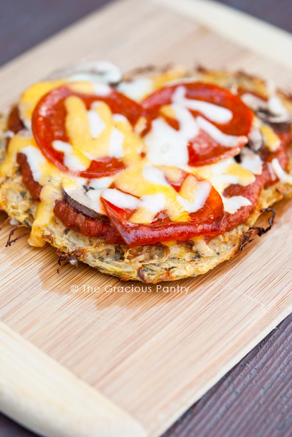 A Clean Eating Single Serving Spaghetti Squash Pizza Crust sits on a cutting board topped with cheese and tomato slices.