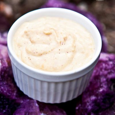 A white bowl of this clean eating taco hummus recipe sits on some amethyst colored rocks for a beautiful, purple background.