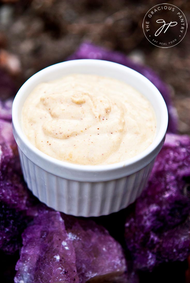 A white bowl of this clean eating taco hummus recipe sits on some amethyst colored rocks for a beautiful, purple background.