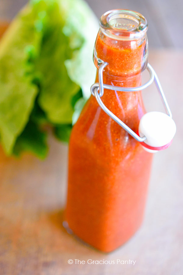 homemade Catalina Dressing in a clear, glass bottle. The attached lid is hanging off to the side to better show the dressing.