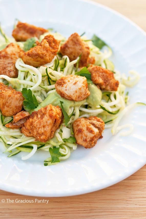 Clean Eating Taco Chicken Zucchini Pasta piled onto a white plate. The zucchini pasta is a bright green and the chunks of chicken are a golden brown color.