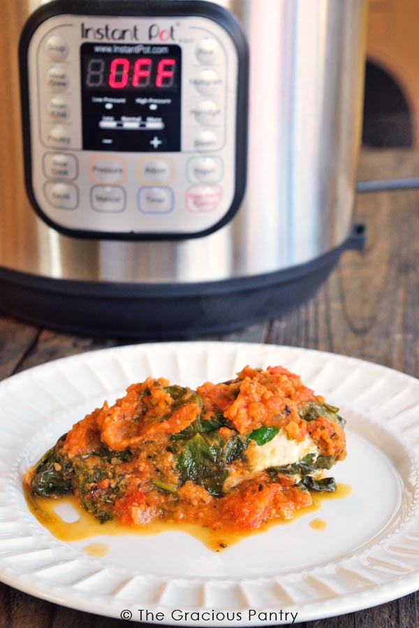 A single white plate holding this Clean Eating Instant Pot Spinach Chicken sits in front of an Instant Pot.