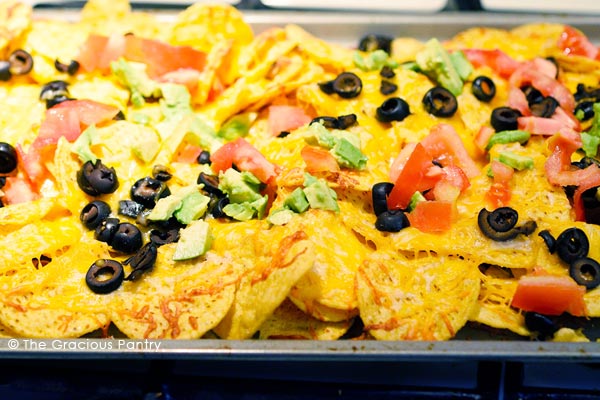 A sheet pan holding loaded nachos topped with chopped tomatoes, avocado and black olives. Just one of the may Friday night dinner ideas in this list.