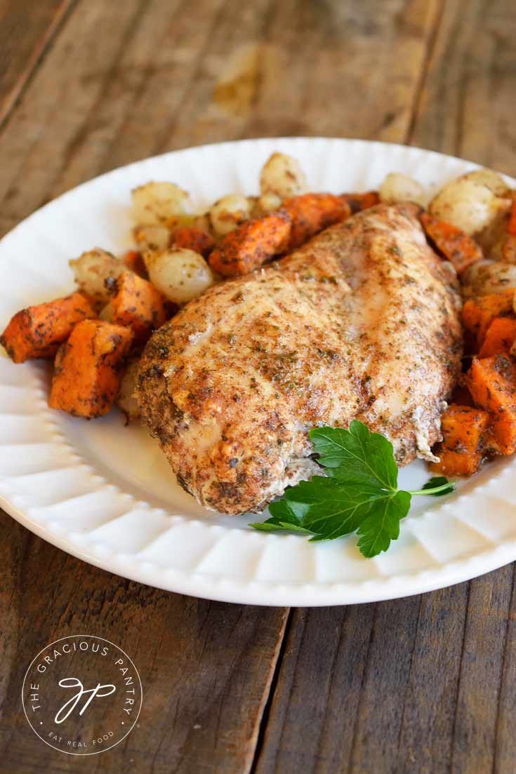 Clean Eating Chicken And Sweet Potatoes Sheet Pan Dinner on a white plate with a bit of green garnish. The chicken and sweet potatoes are evenly covered in spices and have a nice golden hue to them.