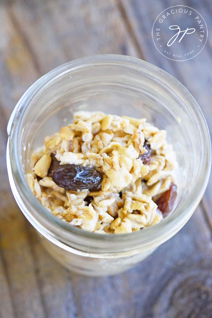 This photo looks down into a small canning jar filled with prepared Clean Eating Oatmeal Cookie Oatmeal. It's filled about half way and you can see the finished oats with a few raisins on top.