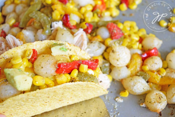 This image shows a taco shell sitting among the vegetables not the sheet pan, stuffed with chicken and veggies and ready to serve.Clean Eating Sheet Pan Mexican Chicken Dinner Recipe