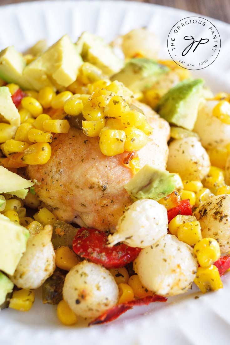 An up close shot of a white plate filled with this Clean Eating Sheet Pan Mexican Chicken Dinner. You can see the chicken, corn, peppers, onions and spices.