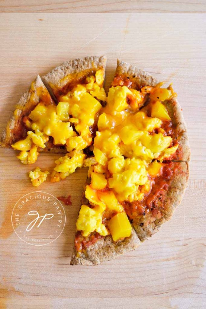A breakfast pita pizza topped with marinara, scrambled eggs, peppers and melted cheese.
