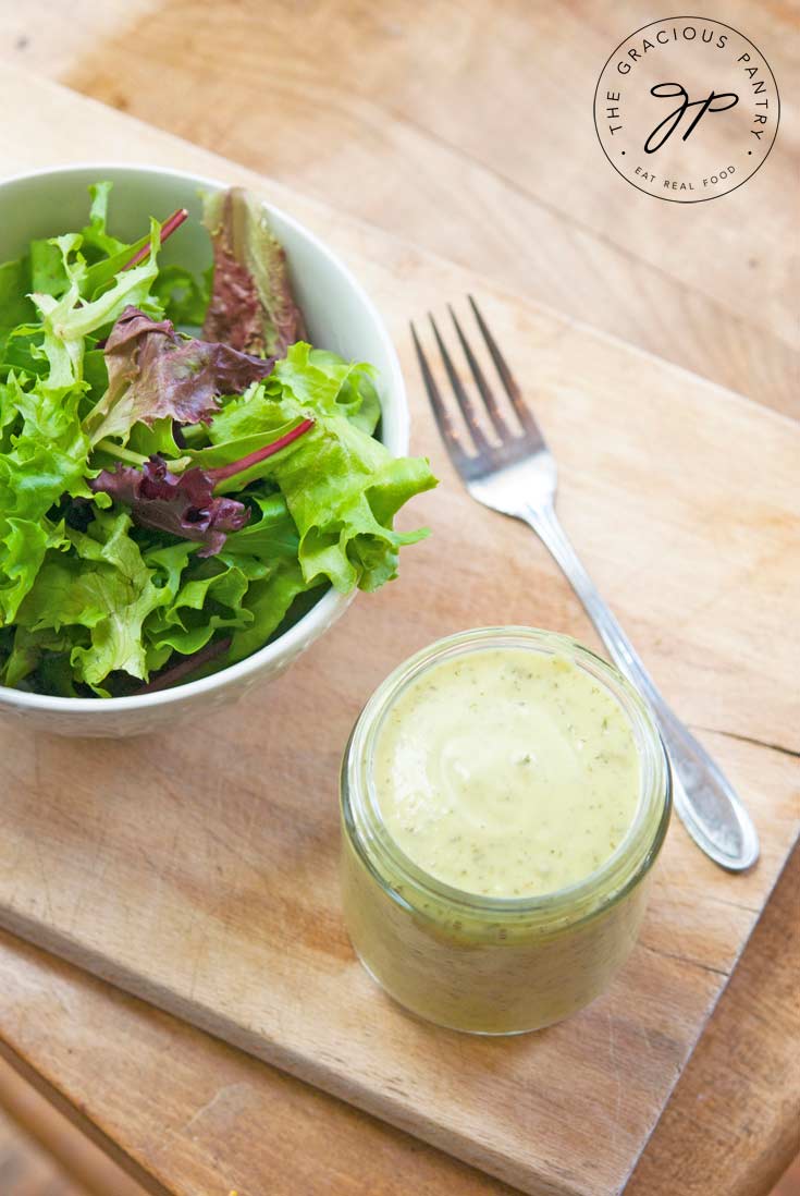 Clean Eating Avocado Lime Dressing in a jar next to a healthy green salad