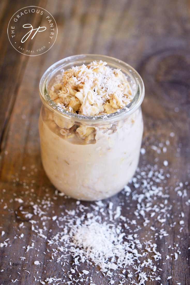 Clean Eating Coconut Bomb Oatmeal Recipe displayed in a clear, glass jar and sprinkled with coconut flakes, ready to serve.