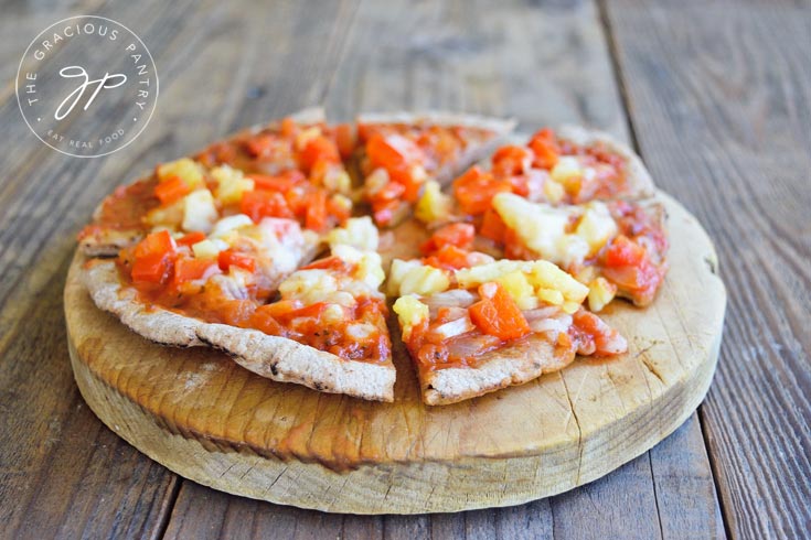 Side view of a Hawaiian pita pizza served on a small round cutting board.