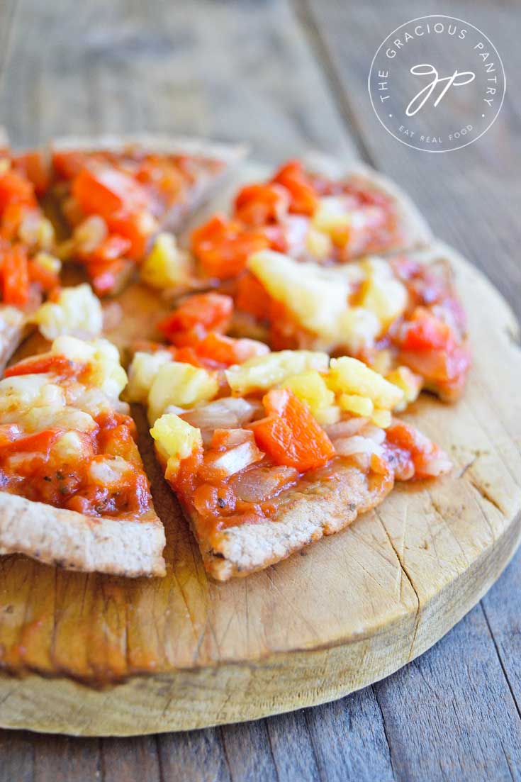 A single, Hawaiian pita pizza cut and ready to eat. Served on a round cutting board.