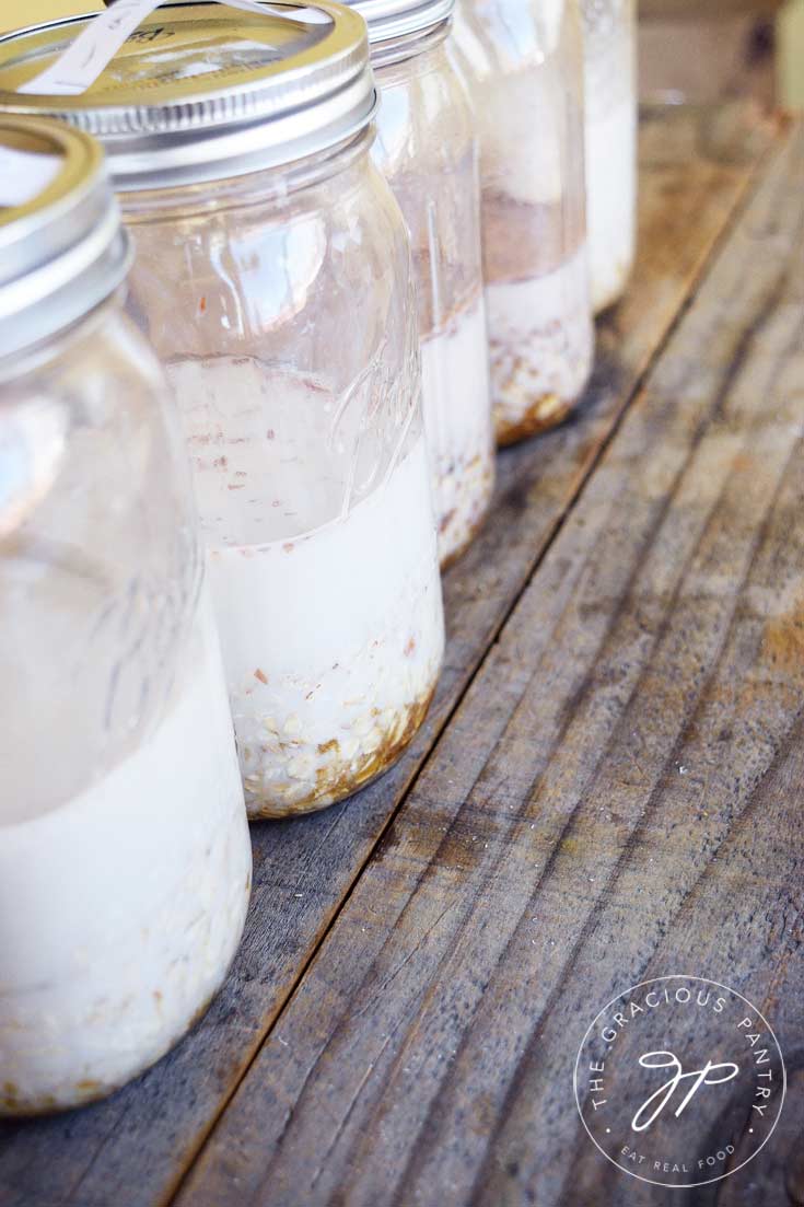 5 jars filled with 5 different Clean Eating Oatmeal Packets of overnight oats. The jars are lined up in a row and have milk mixed in with the oats.