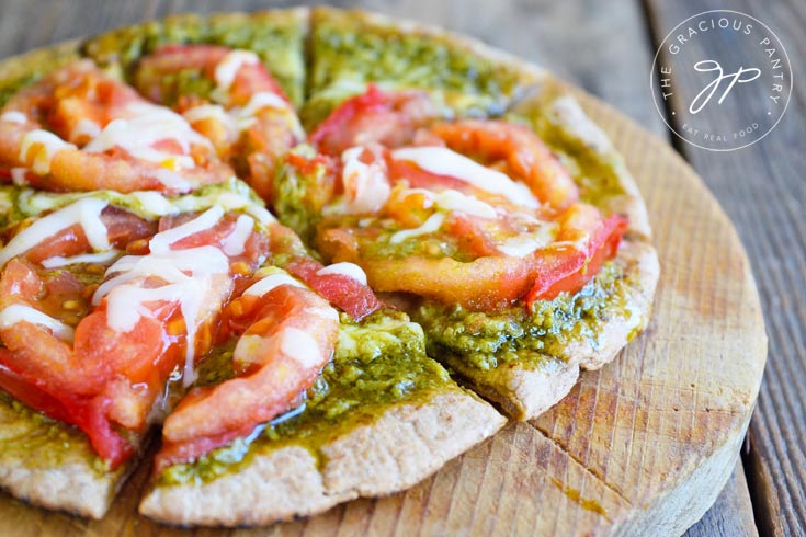 A cut Pesto Tomato Pita Pizza sitting on a round cutting board. One of many Friday night dinner ideas listed in this article.