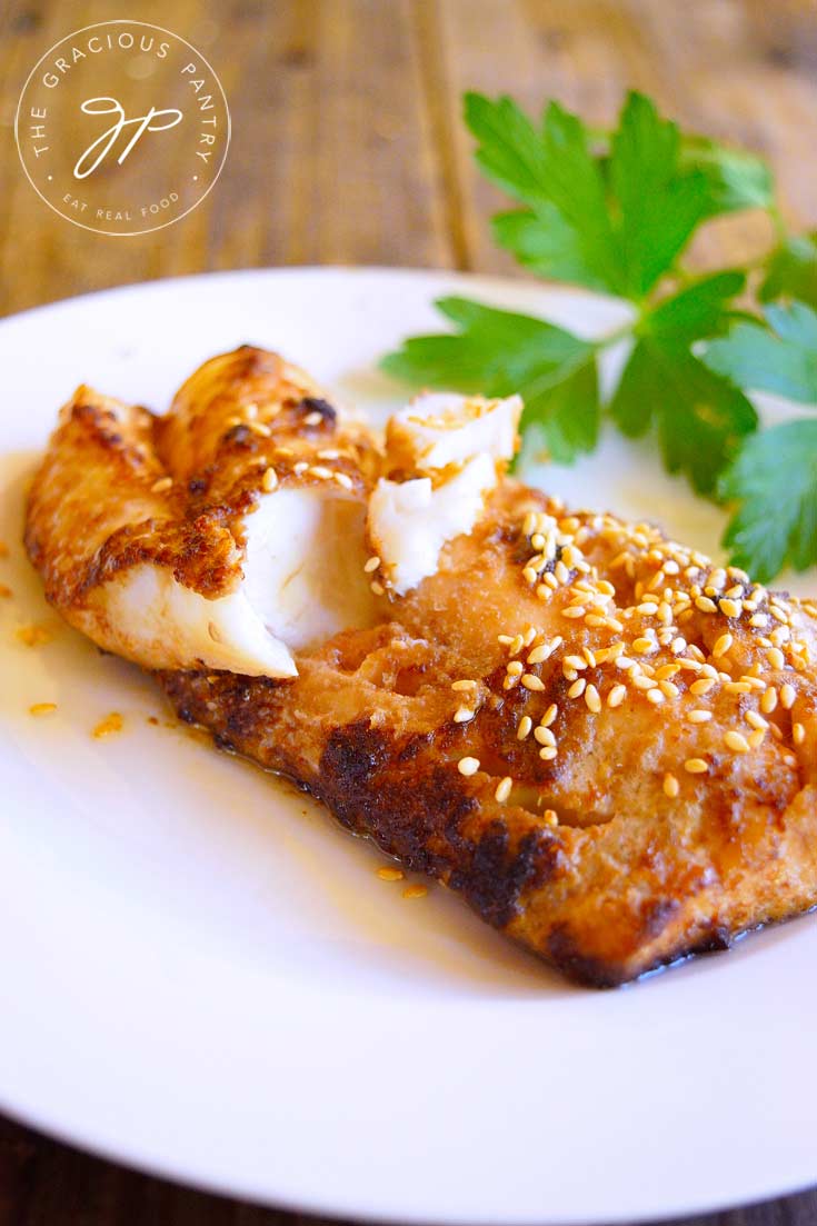 An up close view of this Clean Eating Chinese-Style Sheet Pan Cod Recipe. The fillet is broken in the middle to show the white fish. The outside of the fillet is golden brown and sprinkled with sesame seeds.