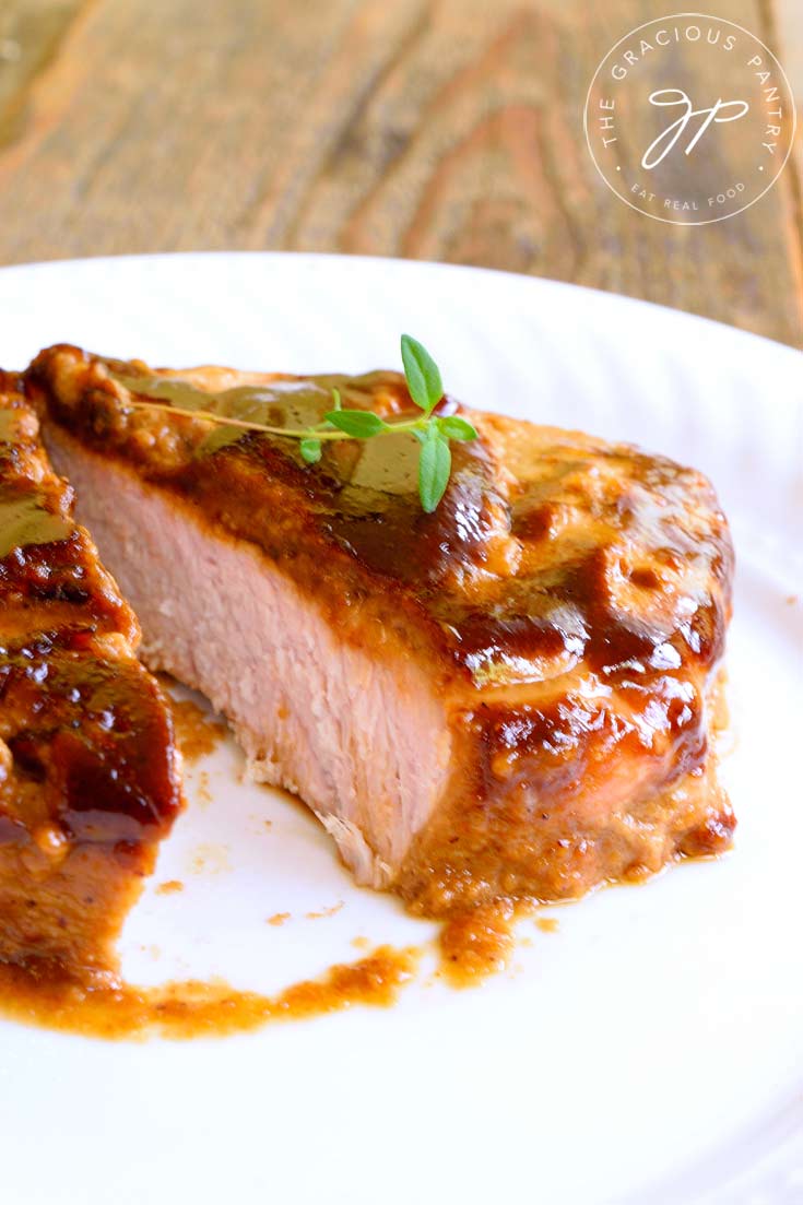A pork chops sits on a white place, covered in a golden brown pork marinade. The meat is cut to show the inside of the chop.