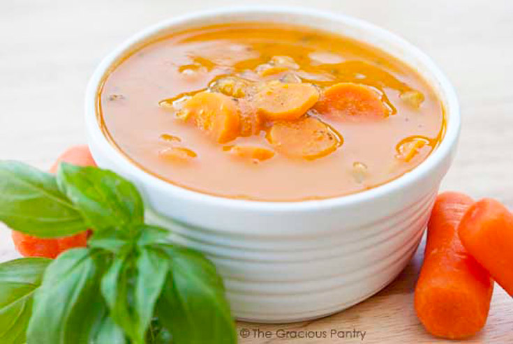 A white bowl filled with an orange/red soup. Carrots lay to the side of the bowl.