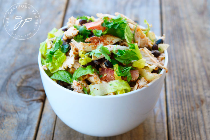 A horizontal shot of a white bowl filled with this salad on a wooden table.