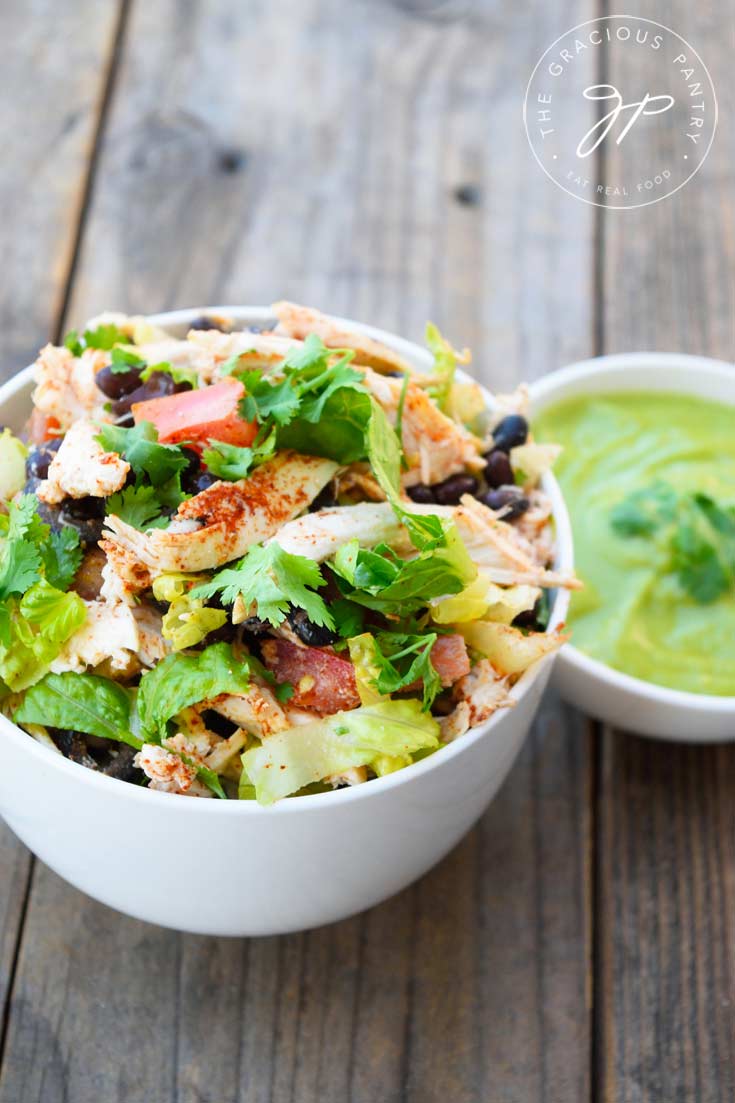 A white bowl filled with this Mexican Chicken Salad Recipe, and a smaller white bowl with dressing sitting to the side on the right.