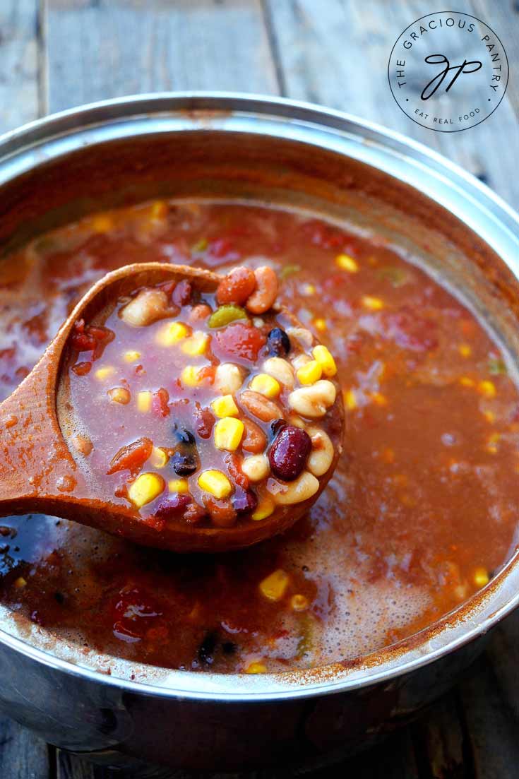 A full pot of Clean Eating Hearty Bean Chowder being ladled out of the pot with a wooden ladle