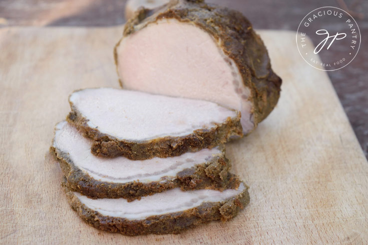 A side view of an herb crusted pork loin sliced and sitting on a cutting board.