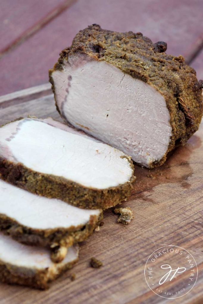 A side view of an herb crusted pork loin laying slice on a cutting board.