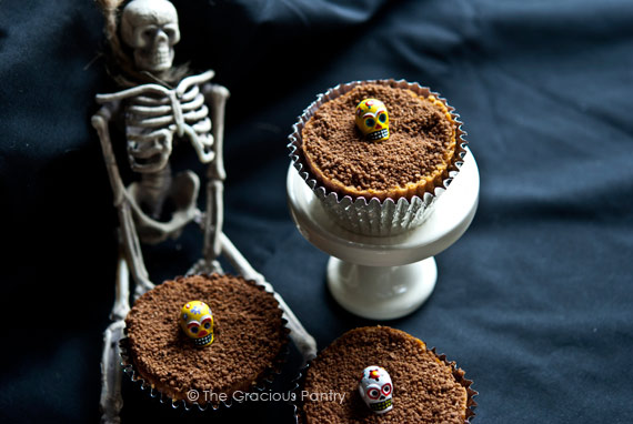 3 Graveyard Dirt Cupcakes displayed on a black background next to a small skeleton.