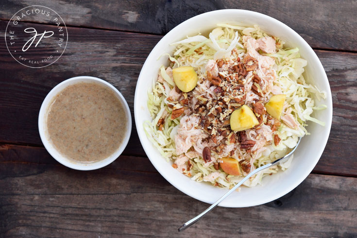 A white bowl filled with Autumn Cabbage Salad and small bowl of dressing sits next to it.