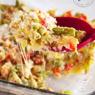 A No Noodle Tuna Casserole sits on a white background. A red serving spoons has scooped up a portion of casserole and it holding it up to the camera.