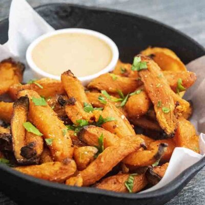 A cast iron skillet filled with fries and dipping sauce.